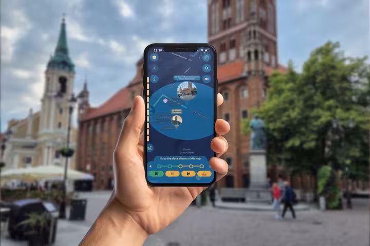 Hand holding smartphone with Copernicus GPS tour app in Torun city square with historic church