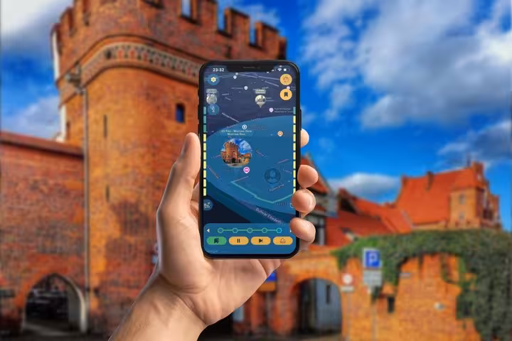 Hand holding smartphone with GPS tour app in front of Torun medieval brick gate tower