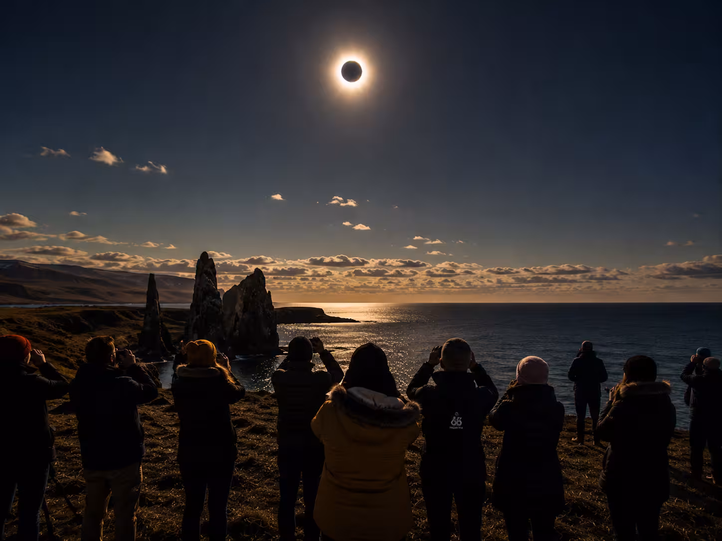 Group watching total solar eclipse over Iceland coastal cliffs and ocean during 2026 eclipse tour
