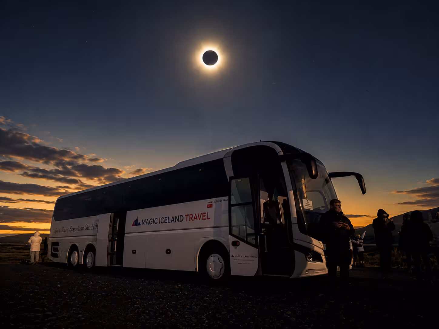 Magic Iceland Travel tour bus parked under a total solar eclipse with glowing corona in dark sky