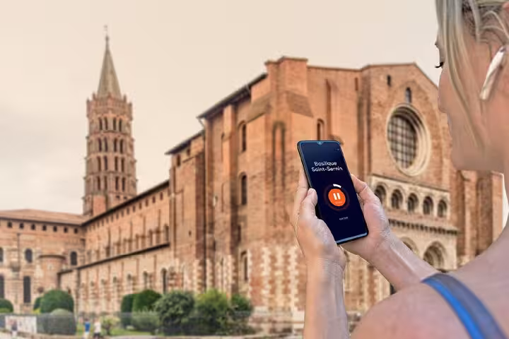 Tourist holding smartphone with audio guide app in front of Basilique Saint-Sernin in Toulouse