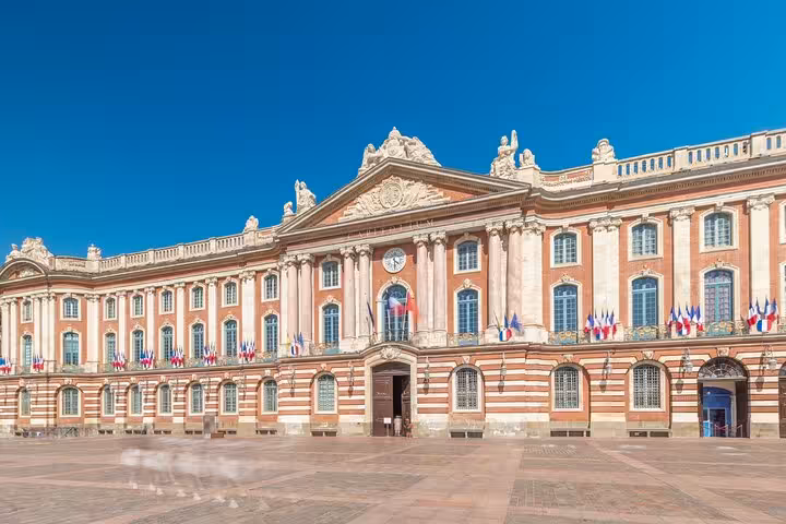 Capitole de Toulouse grand pink brick facade with French flags on sunny day