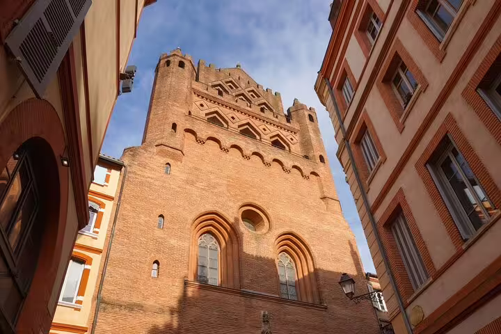 Tall medieval brick tower in Toulouse pink city narrow street viewed from below