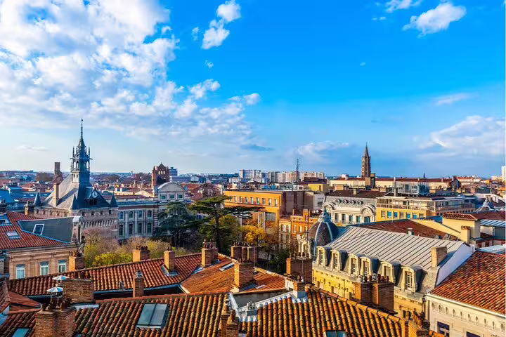 Aerial view of Toulouse pink city rooftops with historic church spires under blue sky