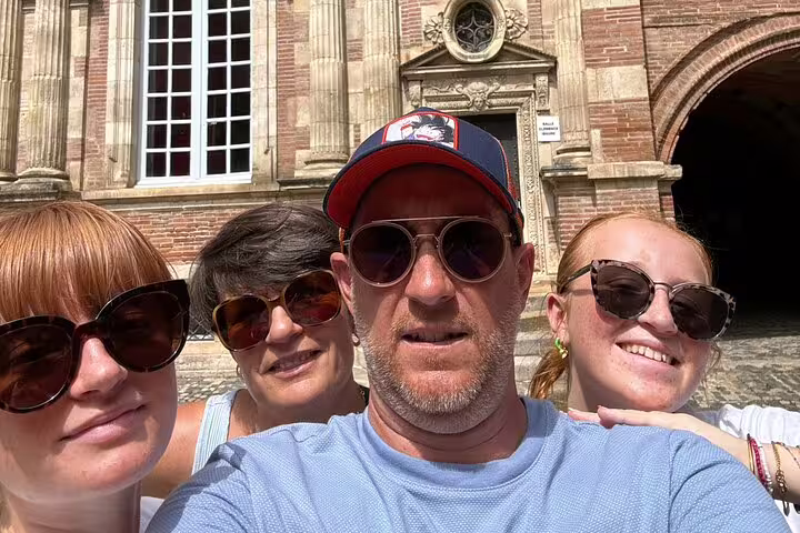 Group of four tourists taking a selfie in front of a historic pink brick building in Toulouse