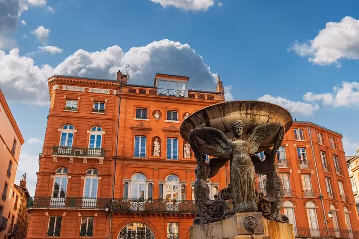 Ornate bronze fountain with angel statue in front of red brick buildings in Toulouse, France
