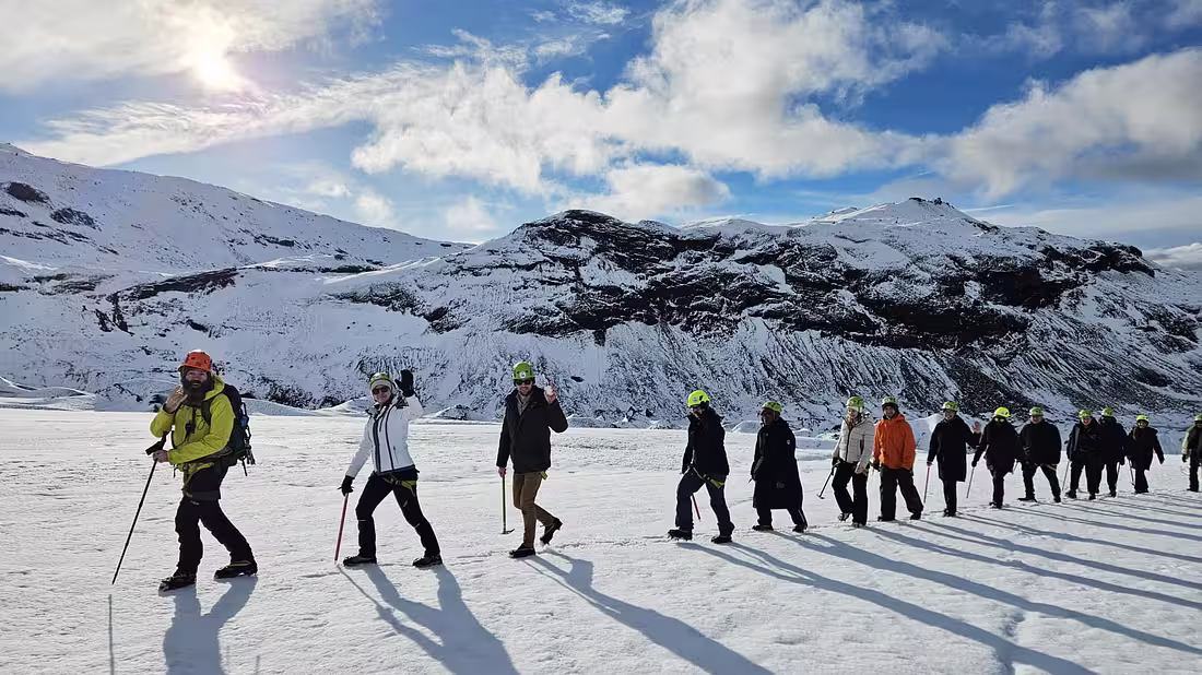 A tour group in hiking gear walking in a line across a glacier