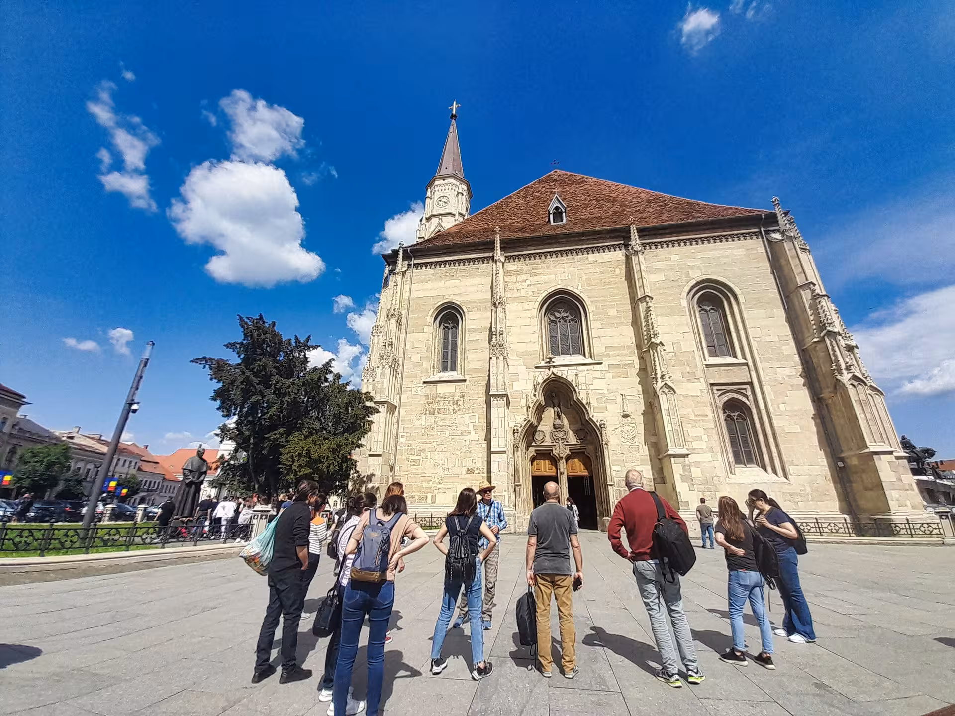 Tour group exploring Gothic Saint Michael Church facade in Cluj Napoca central square on sunny day