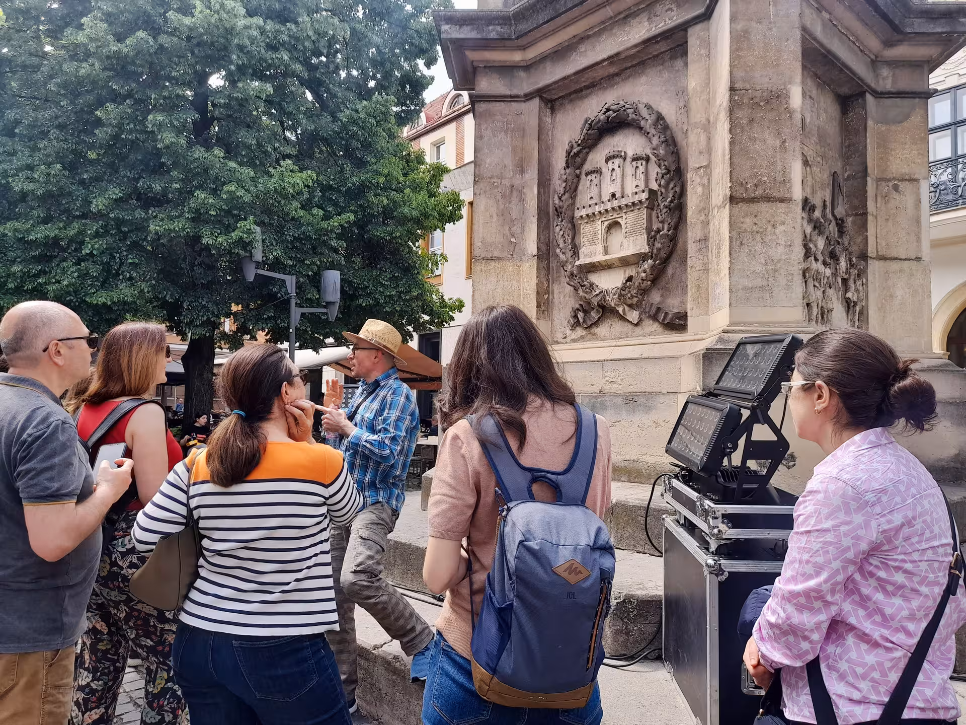 A knowledgeable tour guide explaining the historic coat of arms monument to a group of tourists on a guided walking tour through Cluj-Napoca old town.