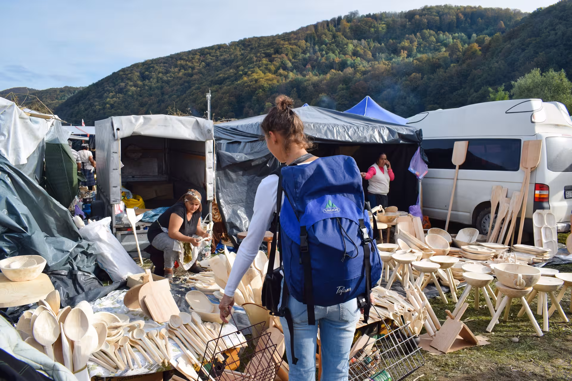 Tourist with backpack browsing handcrafted wooden bowls and spoons at Negreni Flea Market guided tour Romania