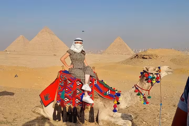 Tourist on decorated camel with Giza Pyramids backdrop on all-inclusive private Cairo Airport shore excursion
