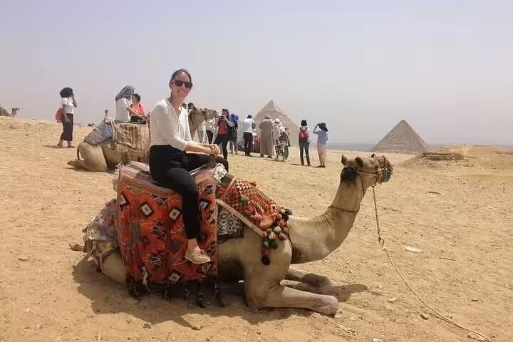 Tourist on camel at Giza Plateau with pyramids in background, half-day private pyramids tour with free ride