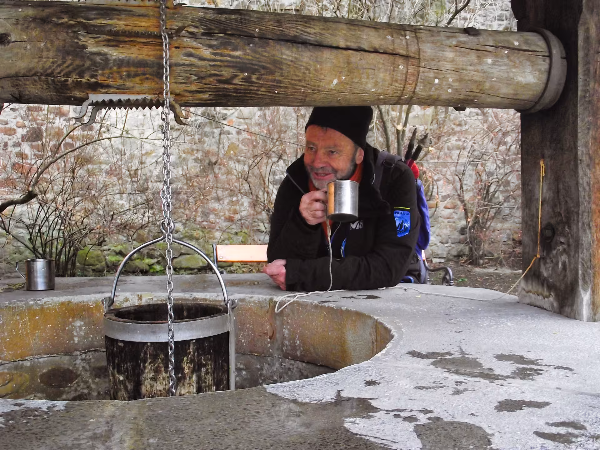 Tourist drinking water from a traditional stone well at a historic Bucovina monastery on an Easter egg painting tour