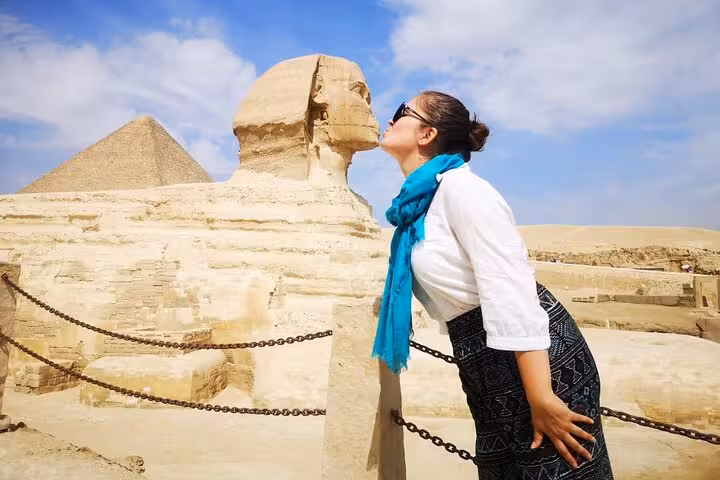 Tourist posing by the Great Sphinx with Giza Pyramid backdrop on Cairo camel ride and lunch tour