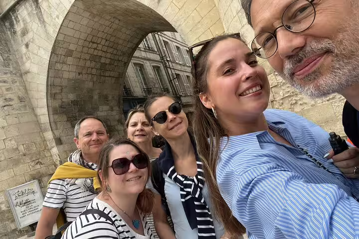 Group of six tourists smiling for a selfie under a historic stone arch in La Rochelle Old Town