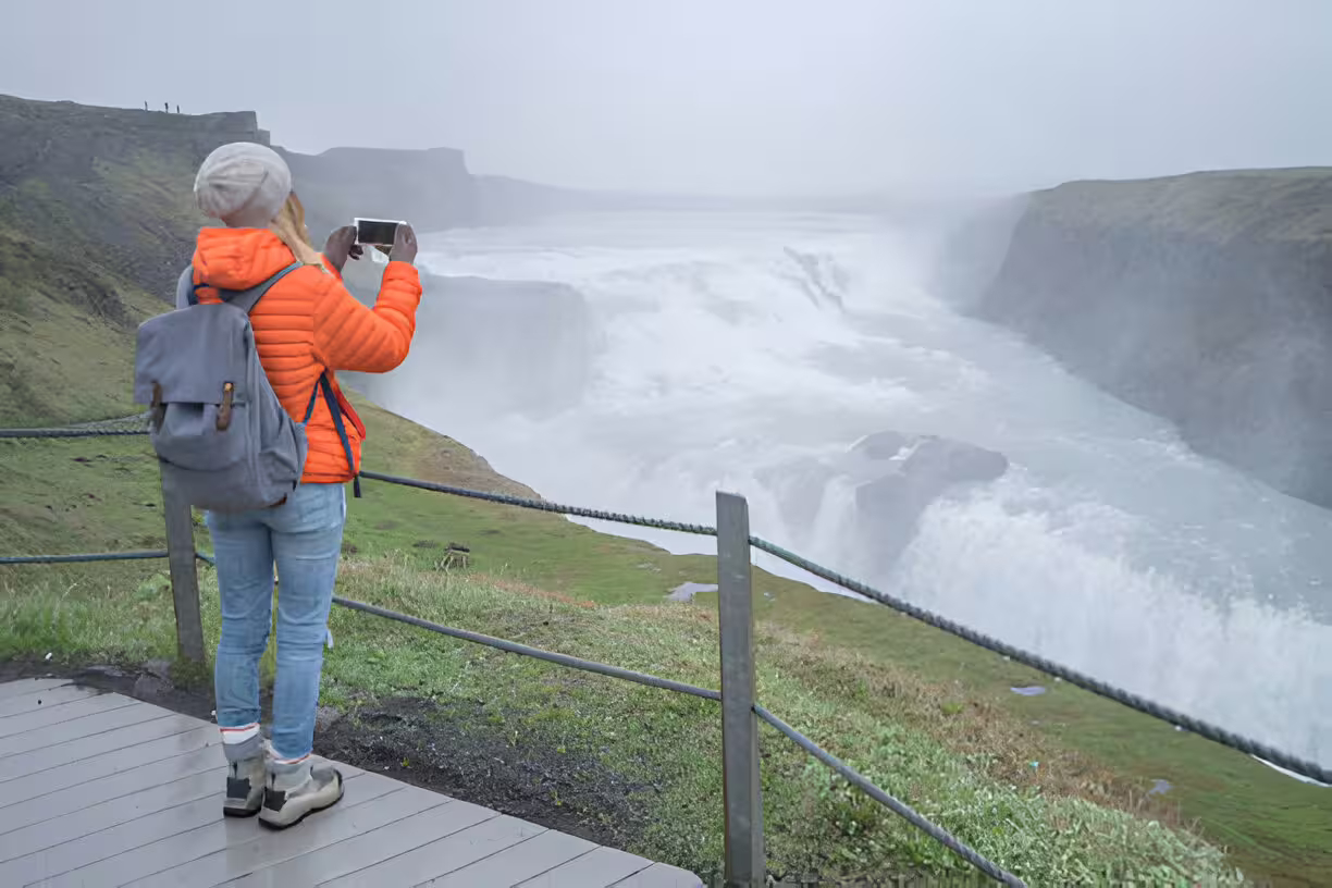 Tourist photographing Gullfoss waterfall on Iceland's Golden Circle tour on a misty day
