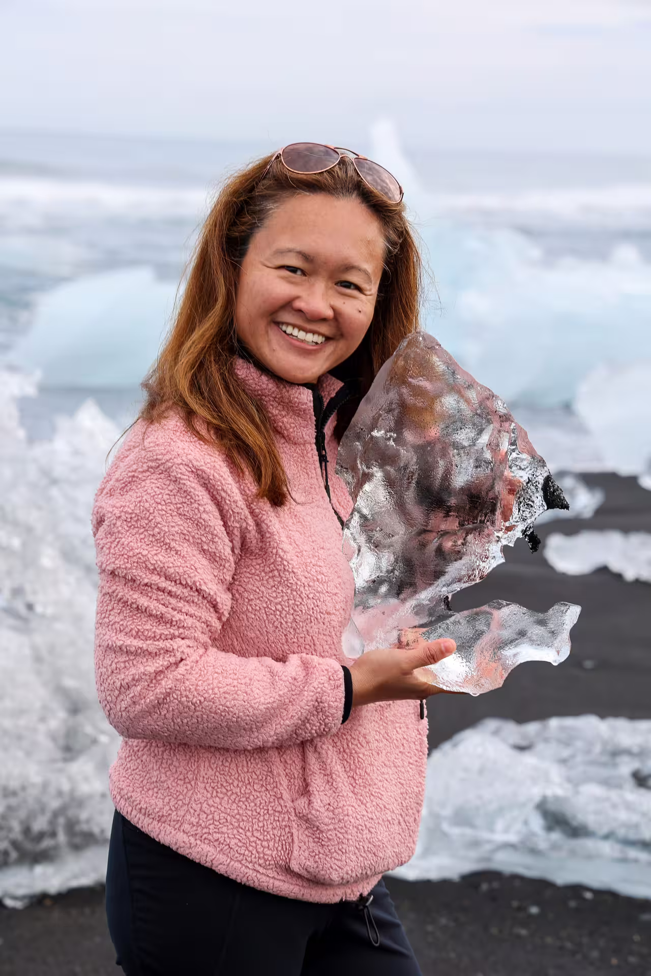 Happy tourist holding a glacial ice chunk on Diamond Beach during Iceland South Coast private tour