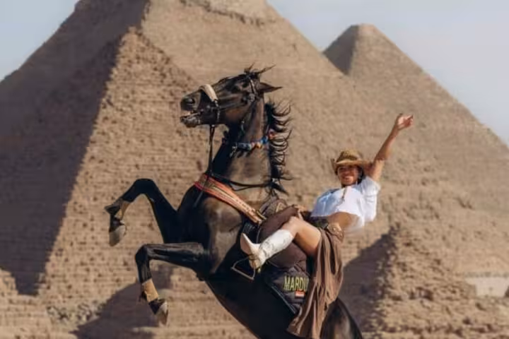 Tourist poses on rearing horse jump photo with Giza pyramids behind on half-day 9-pyramids view tour