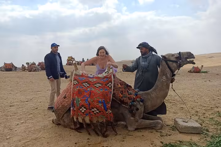 Tourist mounting a decorated camel in the Giza desert on a private pyramids and Sphinx camel ride tour