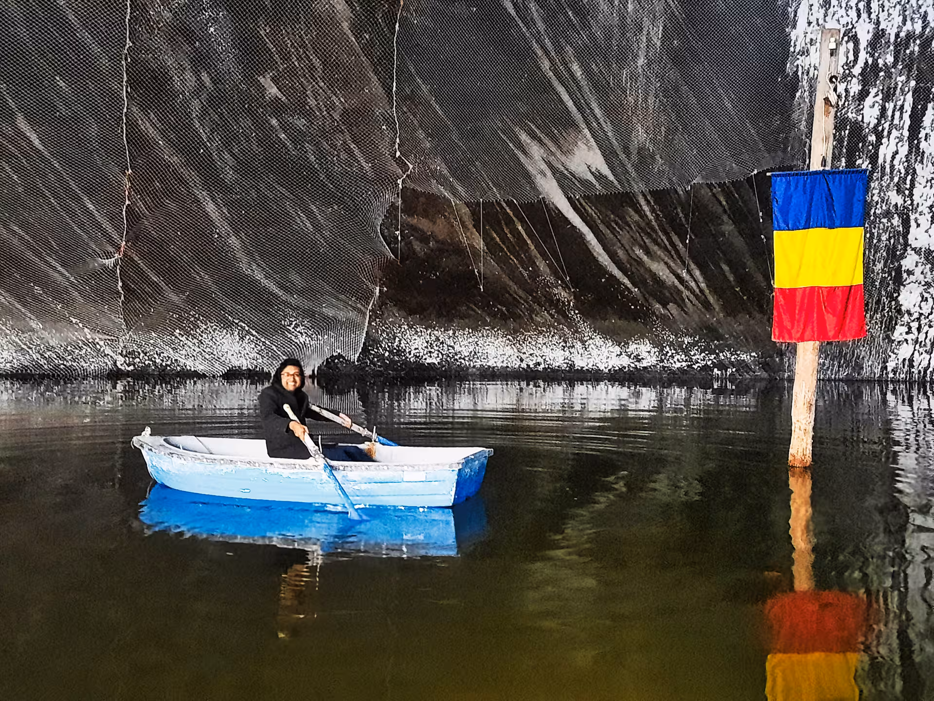 Tourist rowing a boat on the underground lake inside Turda Salt Mine with Romanian flag on a Cluj day trip