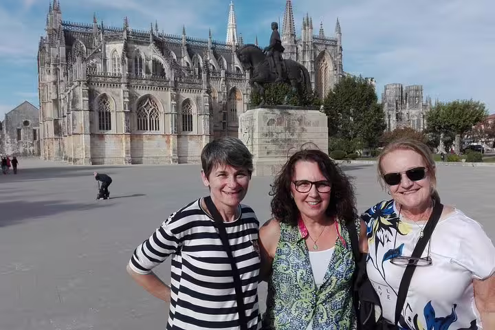 Three tourists pose in front of the stunning Batalha Monastery during a full-day private tour from Lisbon.