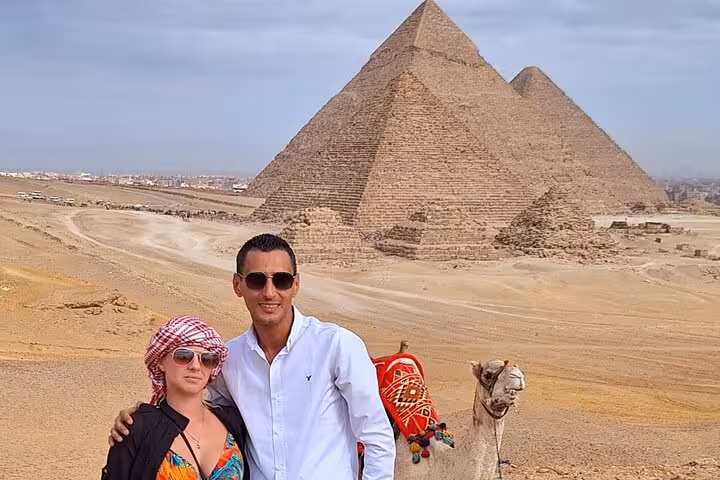 Tourists posing with a camel in front of the stunning Pyramids of Giza during a private guided Egyptian tour.