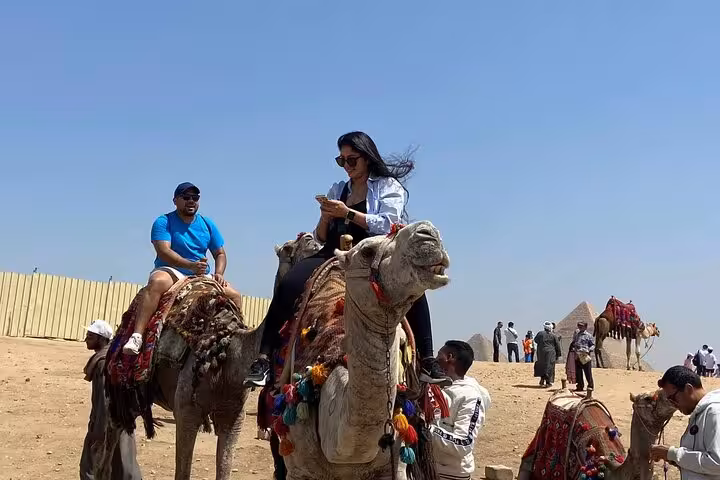 Tourists on camel ride near Giza Pyramids, part of Cairo desert safari with lunch, shopping and quad bike