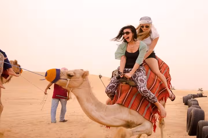Tourists riding camel in desert on super safari trip, included in 5-hour adventure with BBQ dinner and show