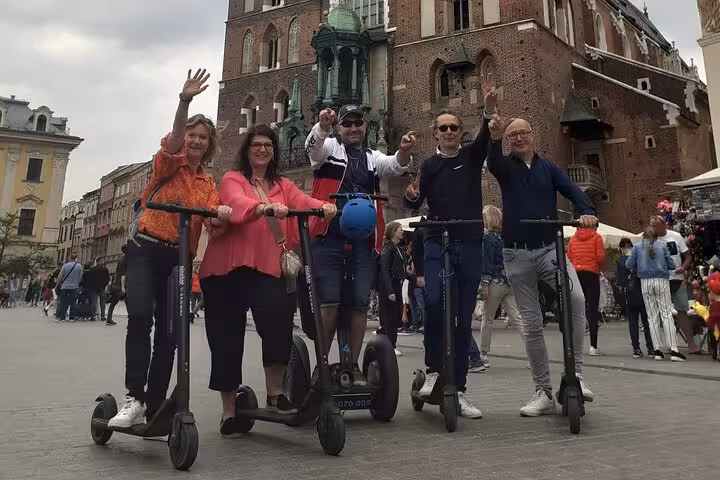 Tourists on e-scooters exploring Krakow's Old Town, posing happily in front of iconic buildings.