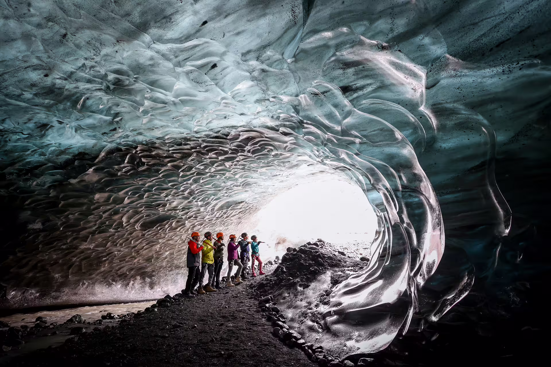 Tourists with helmets exploring a stunning blue Iceland glacier ice cave tunnel on a Viking adventure tour