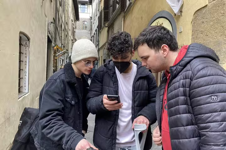 Three young tourists checking a smartphone in a narrow Florence alley during a self-guided walking tour