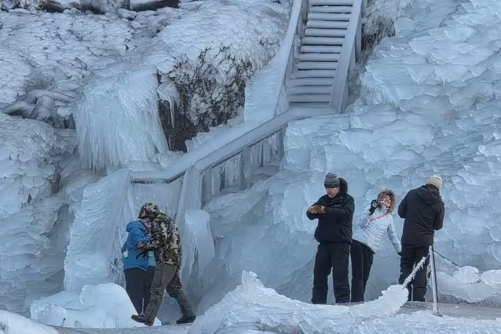 Tourists exploring frozen ice formations on Iceland's south coast near black sand beach in winter