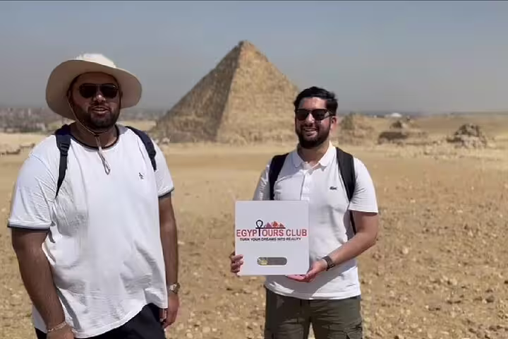 Tourists at Giza Pyramids posing with Egypt Tours Club sign on a half-day pyramids tour in Cairo