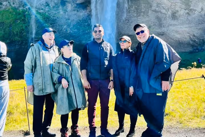 Group of five tourists smiling near a waterfall on Iceland's South Coast day tour