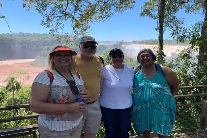 Group of tourists posing at a scenic overlook with Iguazu Falls in the background on a private tour.