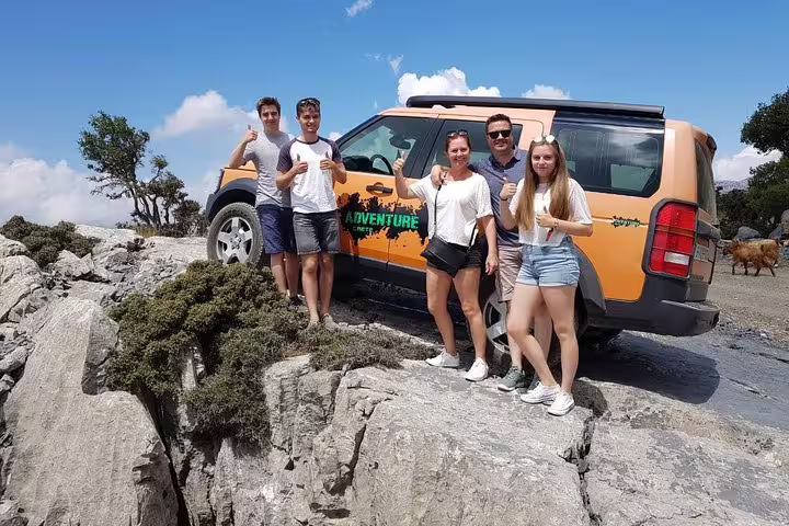 Smiling group of tourists pose beside an adventure jeep on a rocky landscape at Lassithi Plateau, Crete.