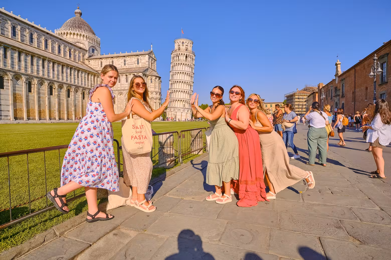 Tourists posing humorously with the Leaning Tower of Pisa on a sunny day during a Tuscany day trip.