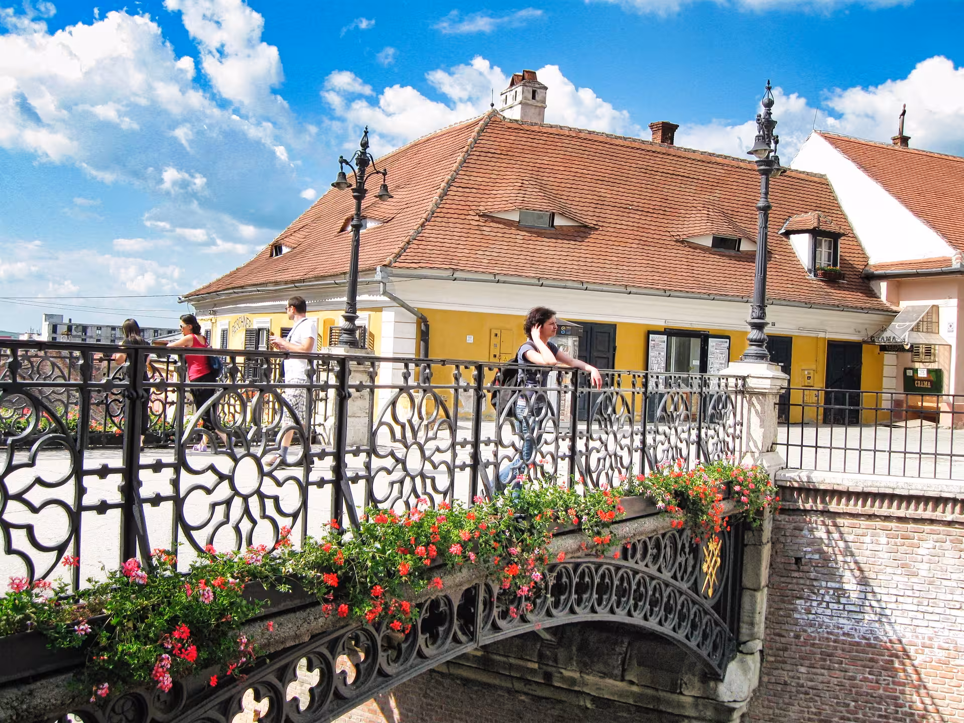 Tourists crossing the ornate flower-adorned Liars Bridge in Sibiu old town on a guided day trip from Cluj-Napoca