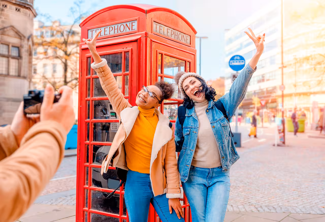 Tourists enjoying a photo moment with a classic red phone booth in vibrant London streets.