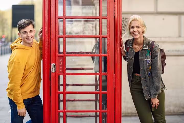 Two tourists smiling by a classic red phone booth in Notting Hill during a private London tour highlighting local markets.