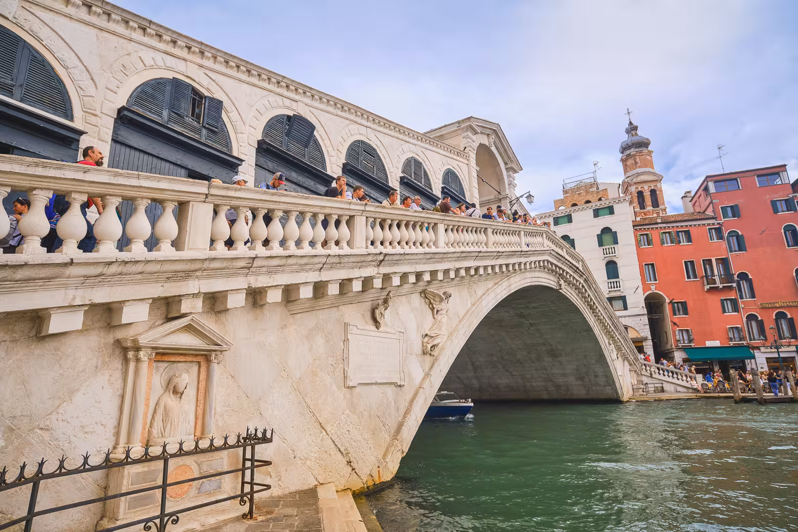 Tourists on Venice's iconic Rialto Bridge over the Grand Canal, featuring classic Venetian architecture and vibrant buildings.
