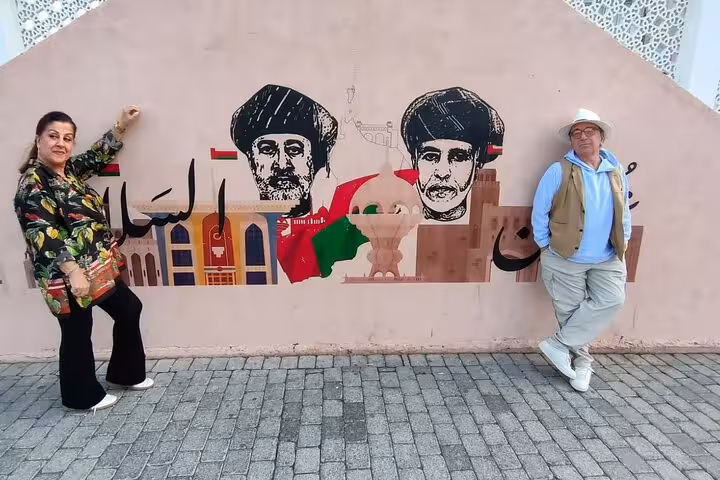 Smiling tourists pose by colorful royal mural in Muscat, capturing Omani culture on a premier classic private cab tour