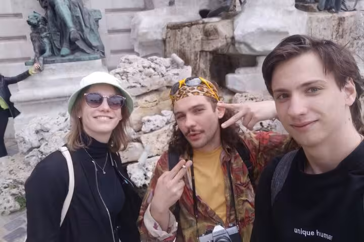 Three young tourists smiling in front of Buda Castle stone fountain sculptures, Budapest