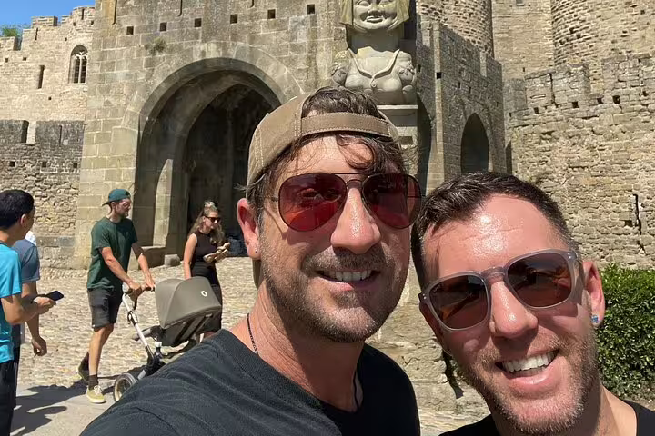 Two smiling tourists taking a selfie at Carcassonne medieval city castle gate entrance on sunny day
