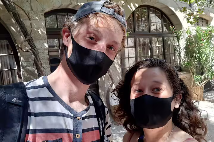 Two tourists wearing black face masks posing for a selfie in front of a historic stone building