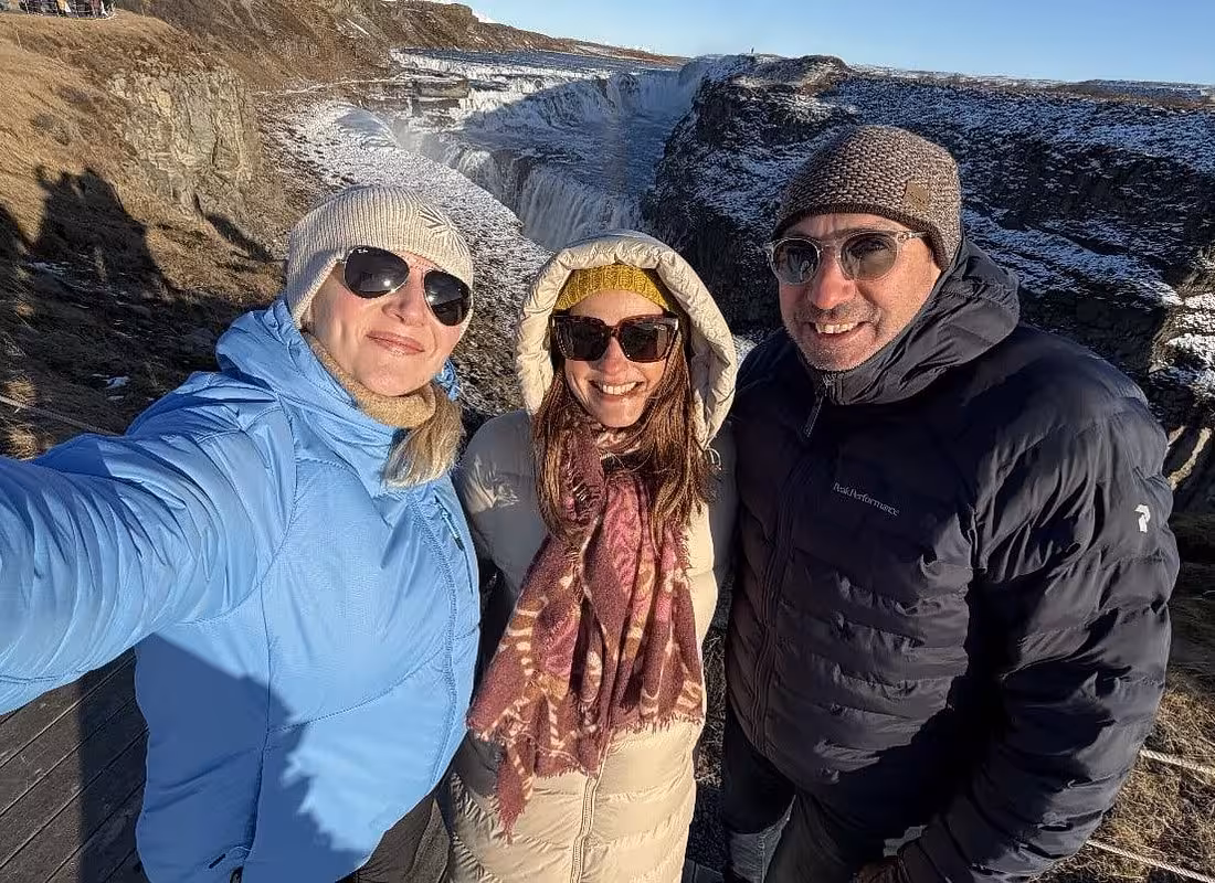 Three smiling tourists in winter gear taking a selfie at Gullfoss waterfall on the Golden Circle tour