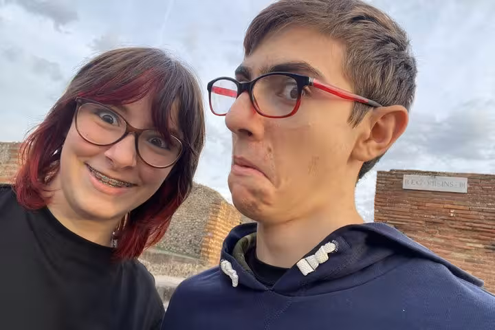 Two young visitors making fun faces at ancient Pompeii ruins during self-guided walking tour