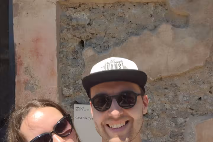 Two smiling tourists in sunglasses posing at Casa dei Cei ruins during a self-guided walking tour in Pompeii