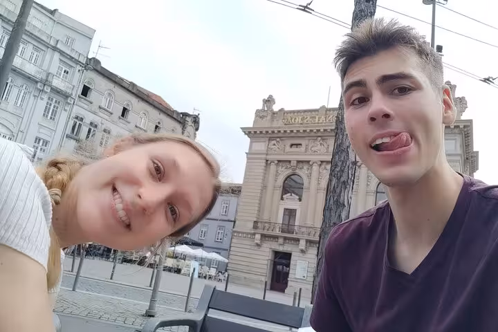 Two young tourists taking a selfie in Porto Old Town square with historic baroque building behind them