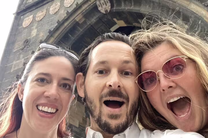 Three tourists taking a selfie in front of a Gothic stone arch in Prague Old Town